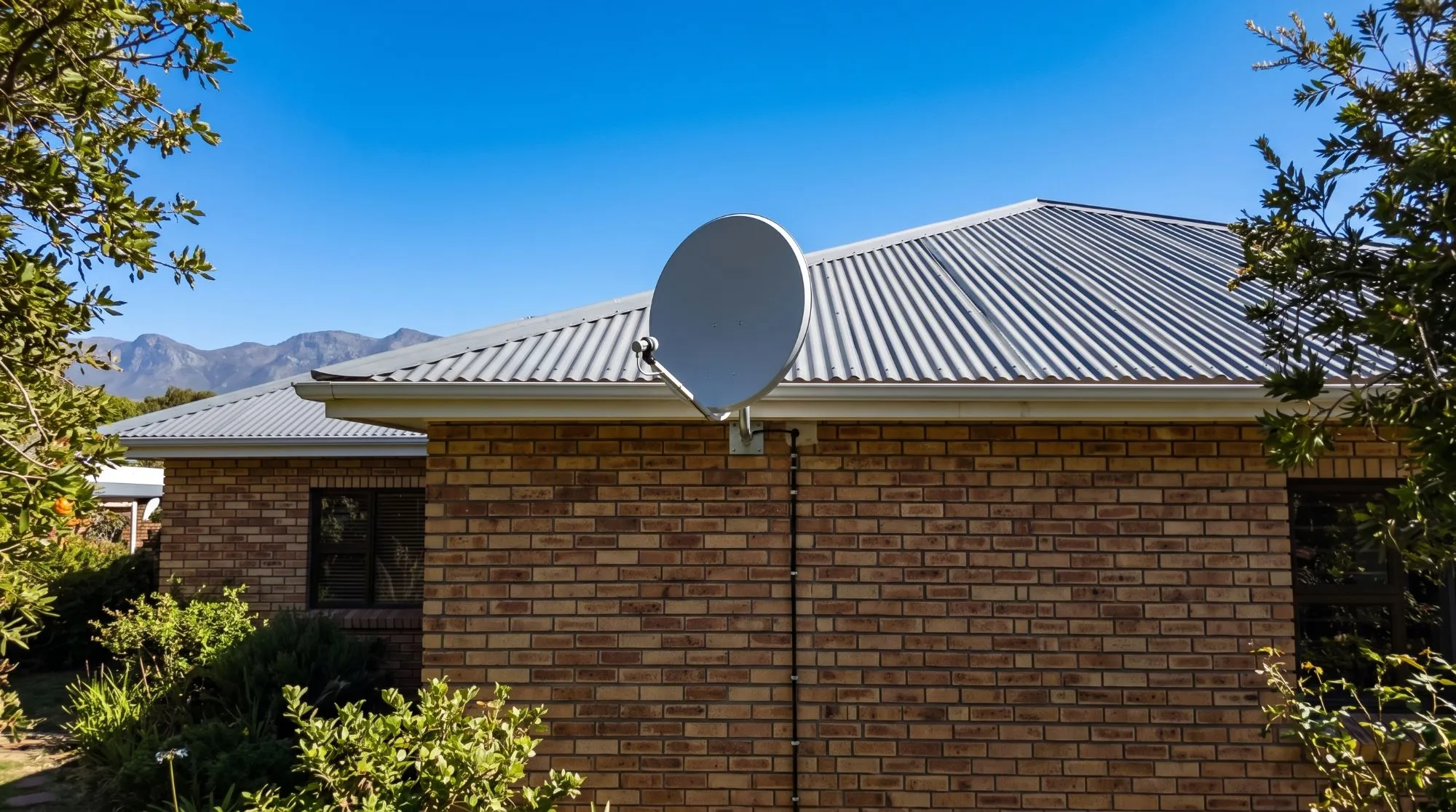 New satellite dish on a galvanised bracket on a brick house, with one neat cable down the wall and mountains behind
